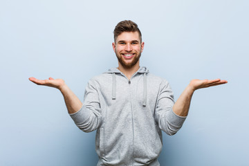 Young handsome fitness man makes scale with arms, feels happy and confident.