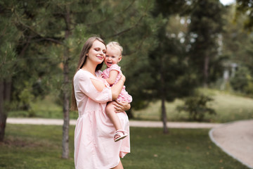 Pregnant woman holding baby girl posing with closed eyes over nature background in park outdoors. Motherhood. Maternity.