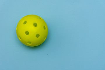 Bright yellow pickleball or whiffle ball on a solid aqua blue flat lay background symbolizing sports and activity with copy space.