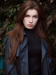 Young adorable redhead woman in black coat with trendy shopper bag emotionally posing in autumn city park with gorgeous red ivy fall leaves background old wooden door