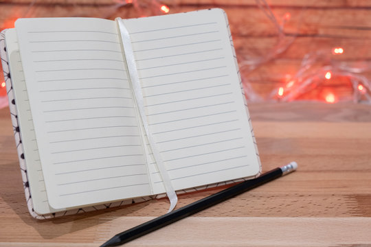 Notebook and pencil on wooden table on background christmas garland - Powered by Adobe