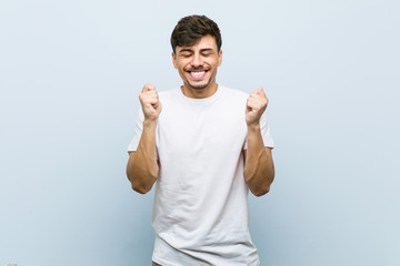 Fototapeta premium Young caucasian man wearing a white tshirt raising fist, feeling happy and successful. Victory concept.