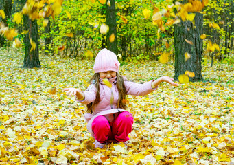 a little girl laughs and plays in the autumn in nature with fallen leaves to walk in the fresh air