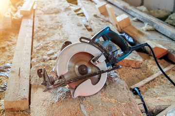 electric portable circular saw is on wooden board in house under construction of foam block