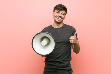 Young hispanic man holding a megaphone smiling and raising thumb up