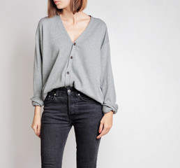 Young woman wearing simple outfit with grey button-up cardigan and black trousers isolated on light grey background. Copy space