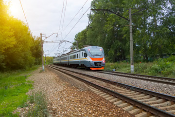 commuter train rides on railway tracks in city with green trees in background