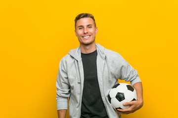 Young caucasian man holding a soccer ball happy, smiling and cheerful.