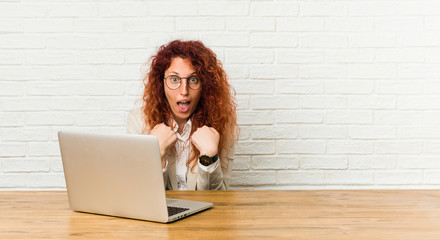 Young redhead curly woman working with her laptop surprised pointing with finger, smiling broadly.