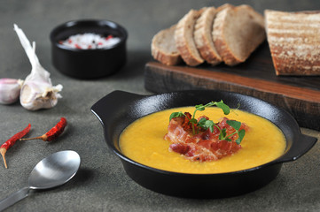 Pea cream soup with bacon. The soup is decorated with green pea sprouts. Slices of brown bread, garlic and spices complete the composition. Dark background. Close-up.