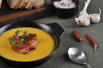 Pea cream soup with bacon. The soup is decorated with green pea sprouts. Dark background. Close-up.