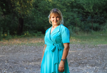A young blonde woman is walking in a city park in a blue dress.