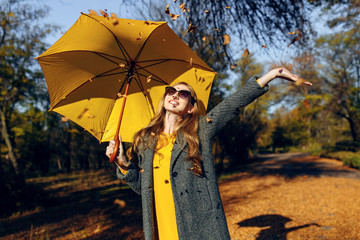 Happy girl, with a yellow umbrella, enjoying the autumn warmth in the Park