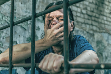 A depressed man holds his hands on the prison bars. Prisoner for the crime. Poor conditions....