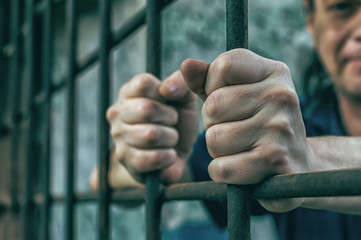 A depressed man holds his hands on the prison bars. Prisoner for the crime. Poor conditions. Scream, despair, pain, hunger.
