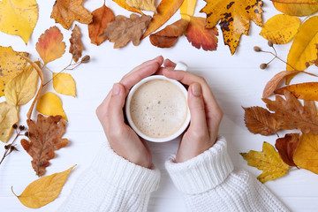 Autumn composition top view. Cup of coffee in the hands and autumn leaves
