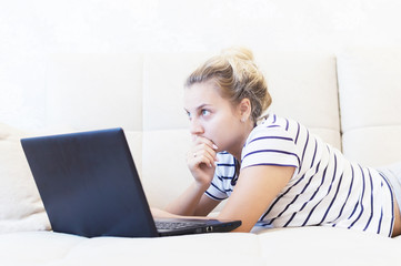 Fototapeta premium blonde girl is sitting at home on the couch with a laptop and communicates on the Internet. social networks. dating.