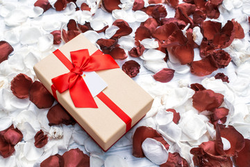 Gift box with dark red and white rose petals on white wooden background. Valentine's background.