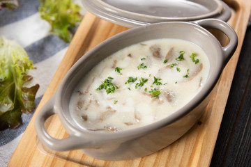 Intense mushroom soup with green vegetables. Beautiful arranged in a grey bowl placed on a wooden chopping board with fresh vegetables. Soup to be eat with a main course for receive complete nutrition