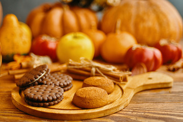 Cookies with pumpkins and apples on the table. Chocolate chip cookies with apples and pumpkins in the background lie on a wooden table.