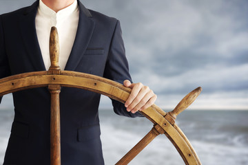 Businessman holding ship wheel and navigates in storm. - obrazy, fototapety, plakaty