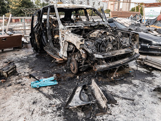A burnt car after a fire or an accident in a parking lot covered with rust and black coal with scattered spare parts around. Robbery, arson, terrorism.