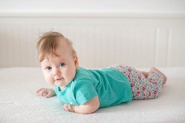 Fototapeta premium Adorable Caucasian baby girl with blue eyes trying to stand up and walk, looking at the camera calmly with a smile; cute baby facial expressions and learning steps or motherhood and family concepts
