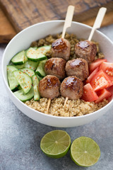 Close-up of a bowl with meatballs on skewers, bulgur, quinoa and vegetables, vertical shot