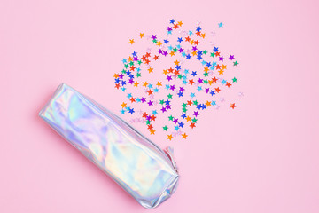 A mother-of-pearl pencil case and multi-colored rhinestones in the form of stars on a pastel pink background. The concept of school supplies, ideas, education. Minimalism. Copy space.