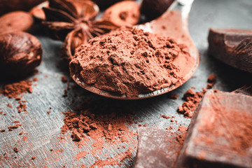 Brown cocoa powder in the spoon, chocolates and nuts, close-up view, selective focus