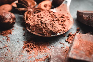 Tuinposter Brown cocoa powder in the spoon, chocolates and nuts, close-up view, selective focus © O.Farion