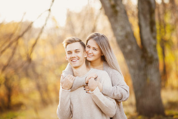 Fototapeta premium Loving couple stands embracing in autumn forest in light beige sweaters, yellow background with leaves