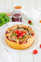 Baked creamy cheesecake with strawberries and crispy shtrezel on a plate on a white wooden background with a cup of tea.