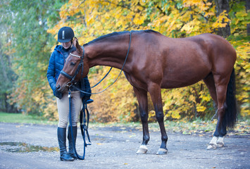Young lady equestrian standing with her lovely chestnut horse