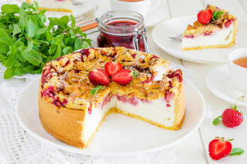 Baked creamy cheesecake with strawberries and crispy shtrezel on a plate on a white wooden background with a cup of tea.