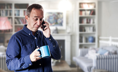 Man in casual blue shirt in the living room using a phone with cup of coffee