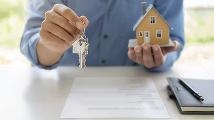 Real estate agent holding a key and asking costumer for contract to buy, get insurance or loan real estate or property.