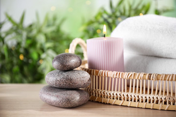 Spa stones and tray with towels and lit candle on wooden table, space for text