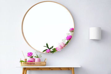 Round mirror and table with accessories near white wall in modern room interior