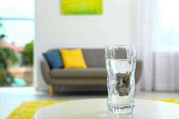 Glass of water on table in room, space for text. Refreshing drink