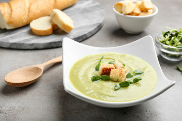 Bowl of broccoli cream soup with croutons and microgreens served on grey table