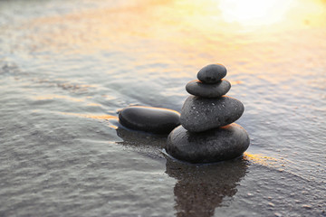 Obraz na płótnie Canvas Dark stones on sand near sea at sunset, space for text. Zen concept