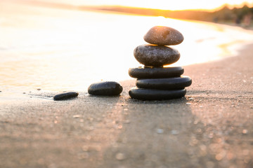 Fototapeta na wymiar Dark stones on sand near sea at sunset, space for text. Zen concept