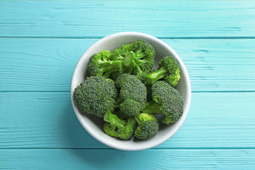Bowl of fresh green broccoli on blue wooden table, top view