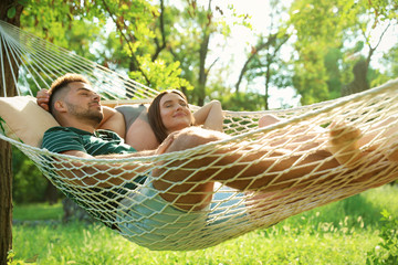 Young couple resting in comfortable hammock at green garden - Powered by Adobe
