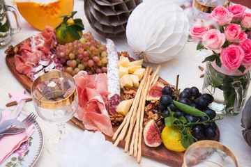 Cheese and charcuterie serving board with parmesan, prosciutto, salami, grapes, figs, bread, pecan nuts, ham and bread sticks. Roses, pumpkin and paper balloons are on the background.