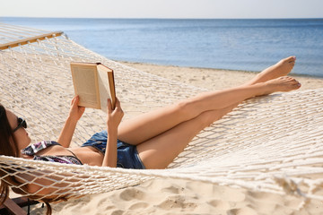Young woman reading book in hammock on beach