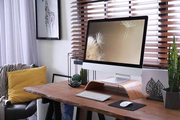 Comfortable workplace near window with horizontal blinds in room