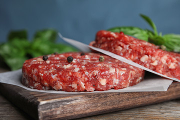 Raw meat cutlets for burger on wooden table against blue background, closeup