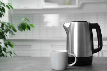 Modern electric kettle and cup on grey table in kitchen. Space for text
